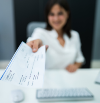 An image of an outsourced payroll manager with her arm stretched out holding a cheque for an employee