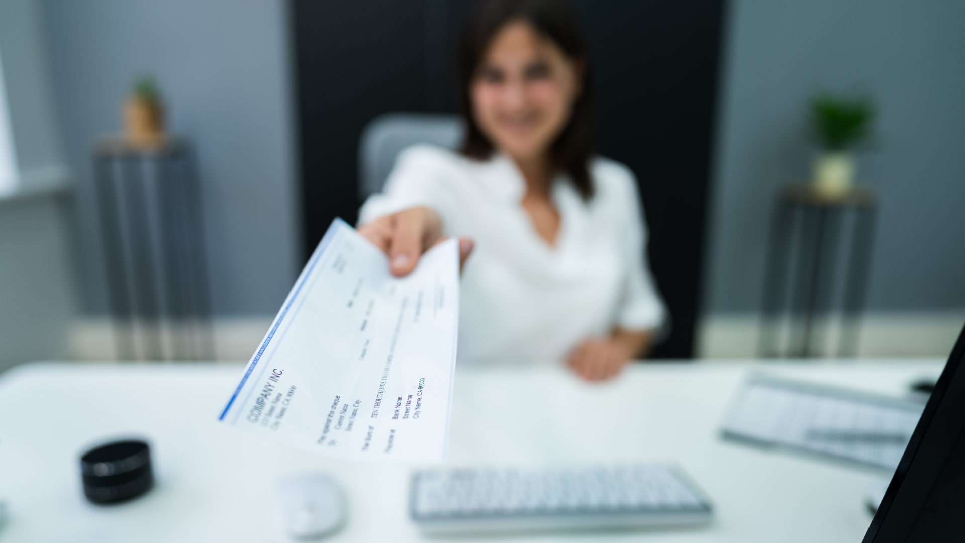 An image of an outsourced payroll manager with her arm stretched out holding a cheque for an employee
